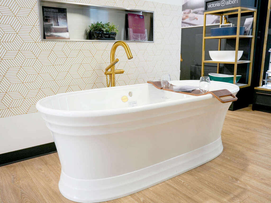 Bain autoportant blanc avec robinet sur pied doré, exposé en salle de montre chez Thalassa Laval